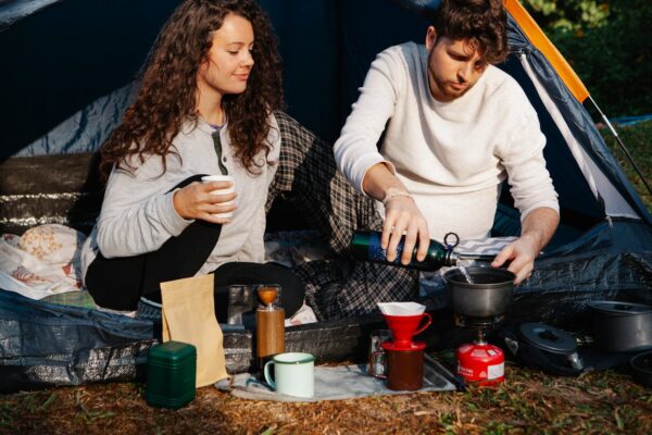 couple de campeurs qui préparent le petit déjeuner devant leur tente.